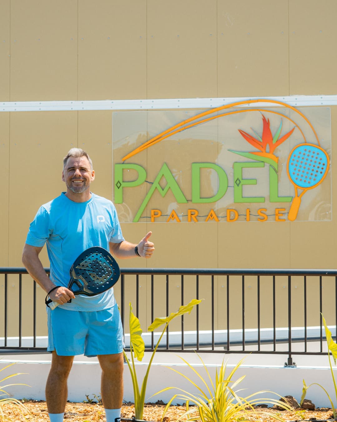 Mathias Laval, pouce levé, devant l'enseigne Padel Paradise