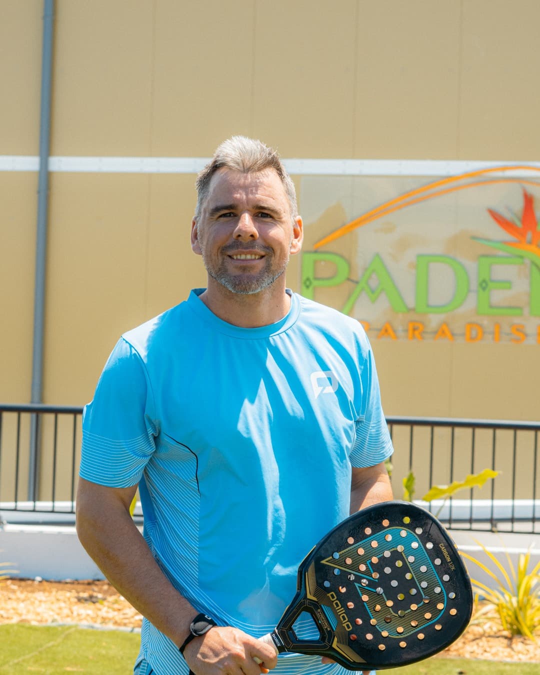 Mathias Laval, coach de padel diplômé d'État, raquette en main devant l'enseigne de Padel Paradise